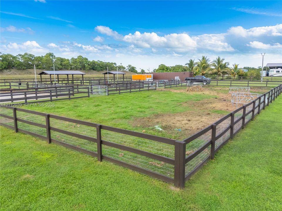 Fenced equestrian grounds featuring multi-section enclosures, metal-roofed structures, and expansive cleared pasture