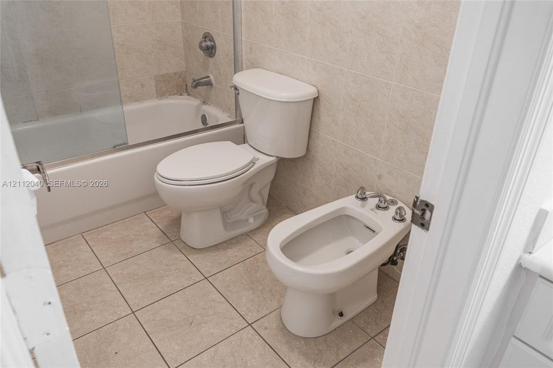 Bathroom featuring a built-in bidet, a two-piece toilet, a porcelain-surround tub with a glass screen, and neutral stone-finish ceramic tile flooring and wall accents