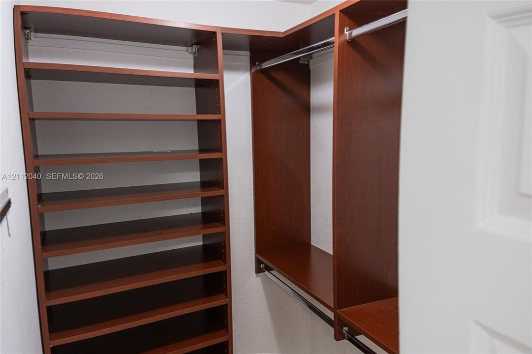 Built-in closet organization system featuring wood-finish cabinetry, adjustable shelving, and integrated metal clothing rods