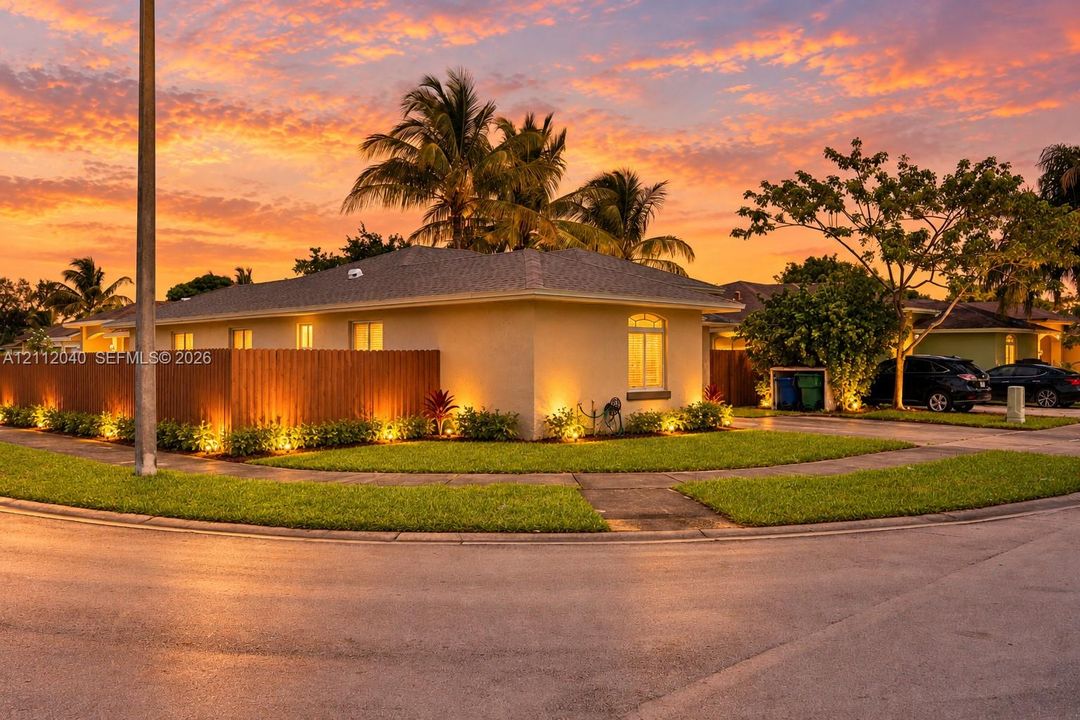 Stucco exterior residence featuring a tall wood privacy fence, integrated landscape lighting, manicured lawn, and mature palm trees