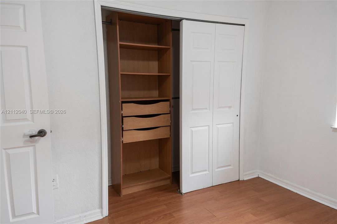 Closet featuring custom wood-finish shelving and integrated storage drawers with white bi-fold doors and wood-finish flooring