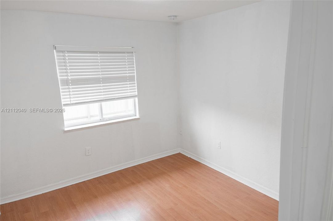Interior space featuring wood-finish flooring, white walls, and a window fitted with horizontal blinds