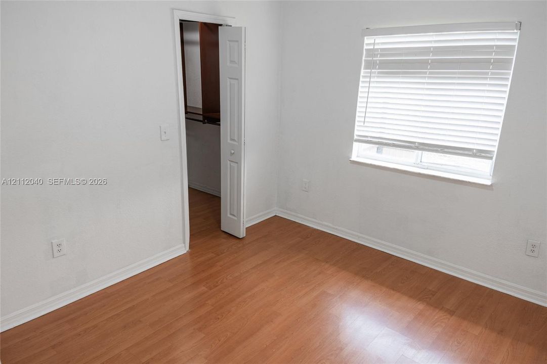 Room featuring wood-finish flooring, white walls, horizontal window blinds, and a closet with a six-panel door