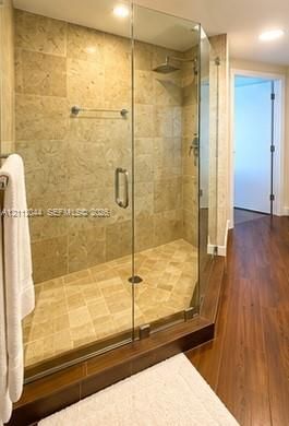 Walk-in shower featuring a frameless glass enclosure, neutral stone tile surround, integrated shower bench, square rainfall showerhead, and wood-finish flooring