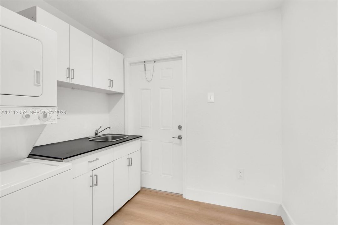 Utility space featuring white cabinetry, a contrasting dark countertop, integrated stainless steel sink with a metallic faucet, and wood-finish flooring