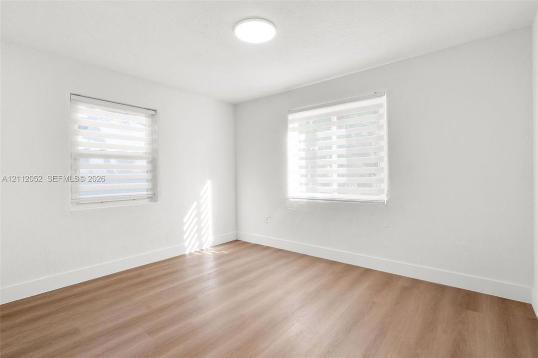 Interior space featuring wood-finish flooring, white walls, two windows with dual-layer fabric shades, and a flush-mount ceiling light fixture