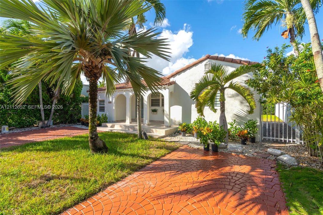 Stucco exterior featuring arched porch entry, clay tile roof, and patterned concrete driveway