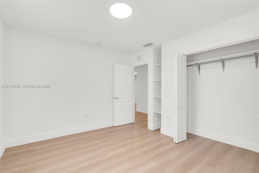 Neutral interior space featuring wood-finish flooring, a recessed ceiling light, built-in shelving, and a closet with a metal clothing rod