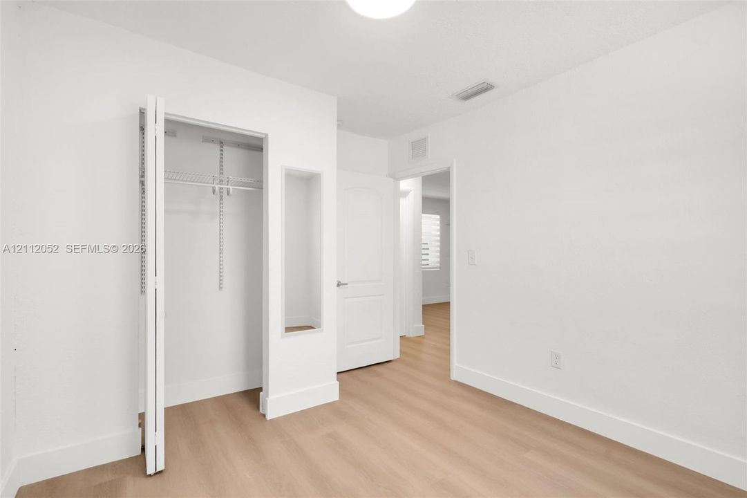 Room featuring wood-finish flooring, a recessed display niche, and a closet with adjustable wire shelving