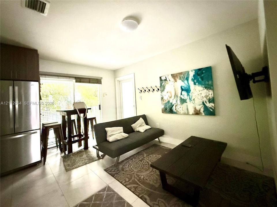 Stainless steel refrigerator, light-colored tile flooring, flush-mount ceiling lighting, wall-mounted coat hooks, and glass sliding door