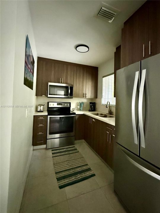 Kitchen featuring custom dark wood-finish cabinetry, stainless steel appliances, a built-in microwave, and solid-surface countertops