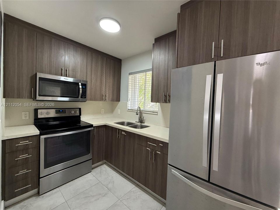Kitchen featuring wood-finish cabinetry, stainless steel appliances, solid-surface countertops, dual-basin sink, and tile flooring