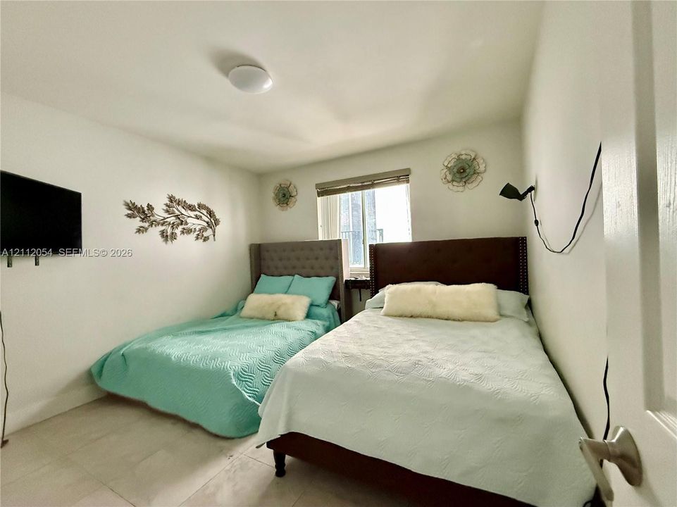 Room featuring white walls, neutral tile flooring, window with a roller shade, and ceiling-mounted dome light