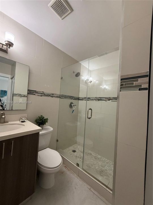 Bathroom featuring a dark wood-finish vanity with a light-toned countertop, a glass-enclosed shower with pebble-tile flooring, and decorative horizontal mosaic tile accents