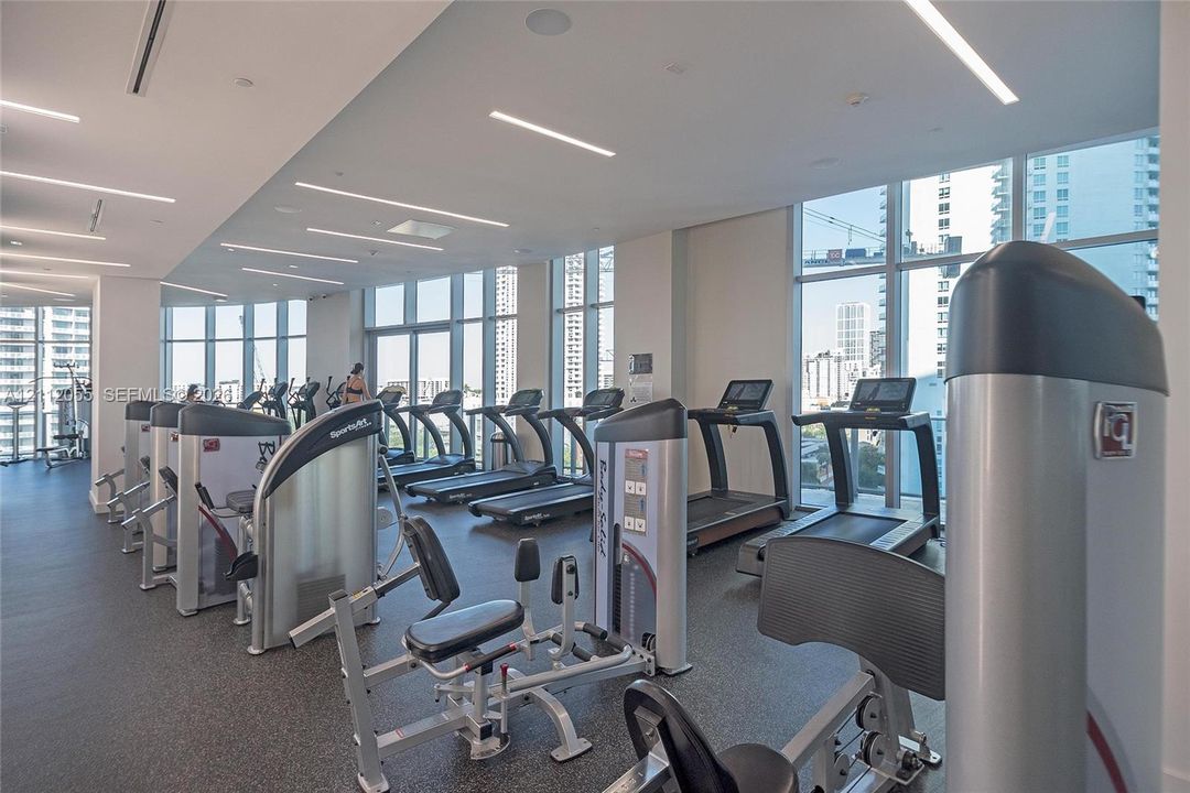 Fitness center featuring floor-to-ceiling windows, high-contrast recessed linear lighting, and integrated ceiling speakers