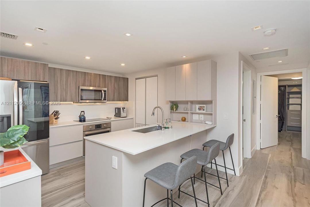 Kitchen featuring wood-finish cabinetry, quartz countertops, stainless steel appliances, a central island with a built-in sink, and wood-finish flooring