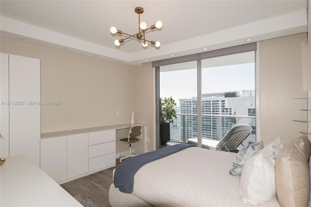 Floor-to-ceiling sliding glass door, built-in cabinetry with integrated desk workspace, wood-finish flooring, and modern multi-arm chandelier