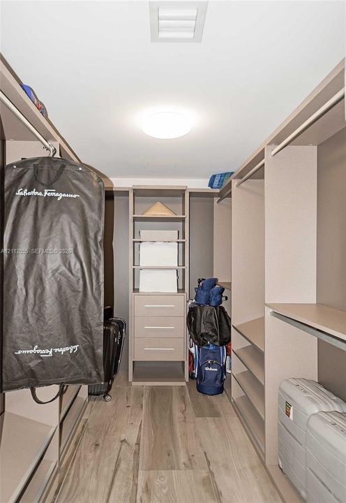 Walk-in closet featuring custom built-in cabinetry, integrated shelving, three storage drawers with metallic hardware, and wood-finish flooring