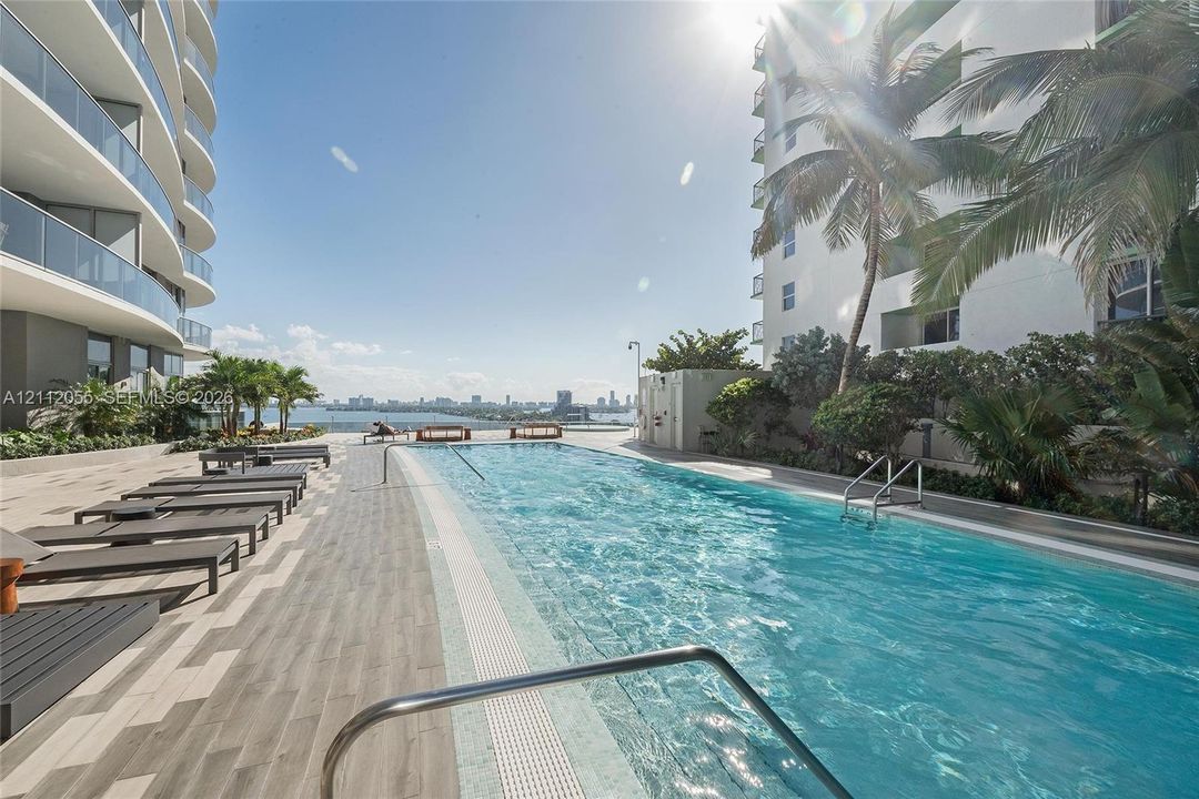 Outdoor swimming pool featuring a tiled deck, water-level tile perimeter, metal handrails, and tropical landscaping