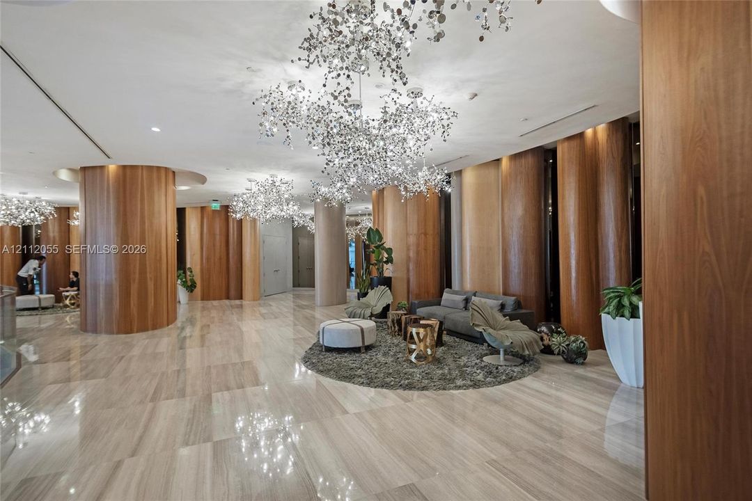 Polished stone flooring, floor-to-ceiling wood-panel accent walls, and ornate metallic sculptural chandeliers