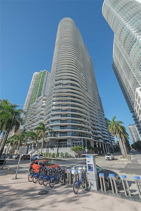 High-rise residential tower featuring a curvilinear architectural design, floor-to-ceiling glass paneling, and wrap-around balconies
