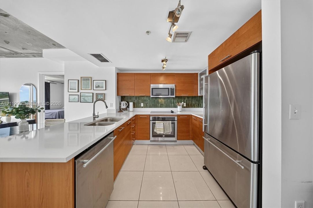 Kitchen featuring wood-finish cabinetry, white countertops, stainless steel appliances, tiled backsplash, and light-tone tile flooring