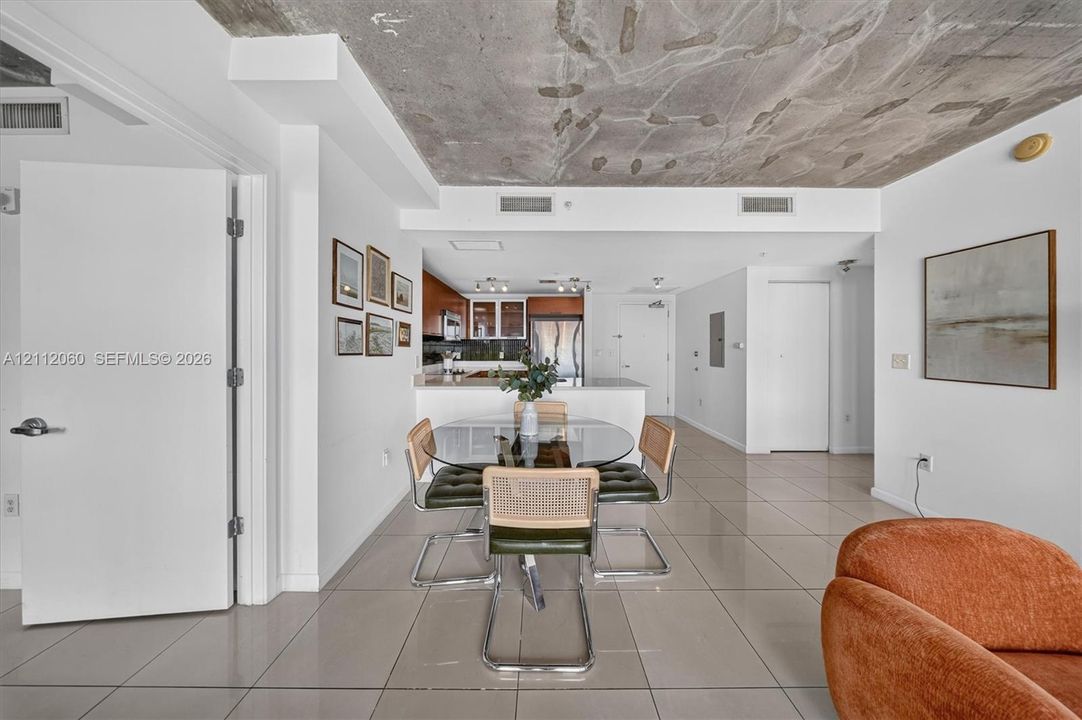 Exposed industrial concrete ceiling, polished large-format tile flooring, and integrated kitchen cabinetry featuring a quartz-topped peninsula