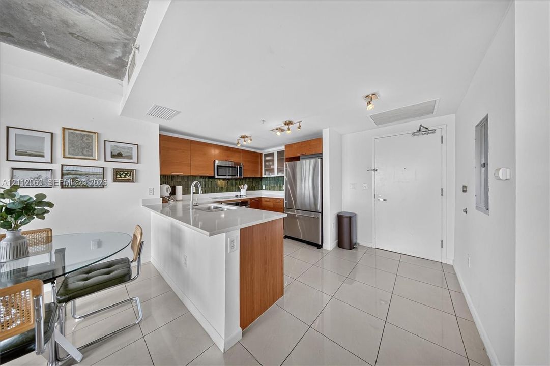 Kitchen featuring wood-finish cabinetry, stone-surface countertops, tile flooring, stainless steel appliances, and exposed concrete ceiling detail