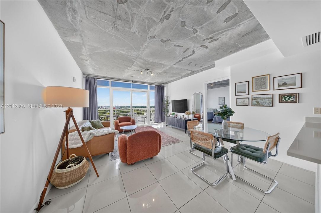 Exposed concrete ceiling, large-format tile flooring, and floor-to-ceiling glass sliding doors opening to an exterior balcony