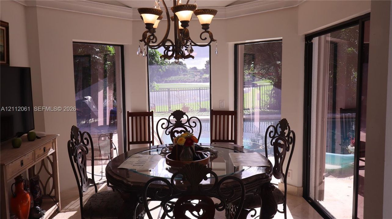 Spacious breakfast area featuring large floor-to-ceiling windows opening to lake view, crown moulding, Italian chandelier, and sliding glass doors leading to the exterior