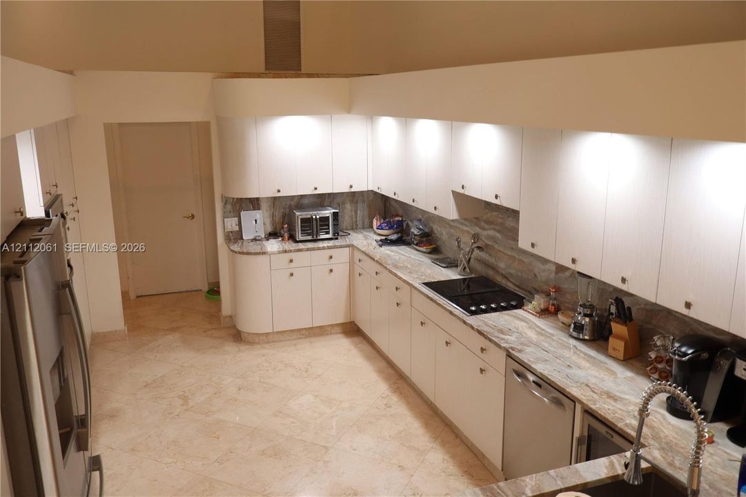 Kitchen featuring light wood laminate cabinetry, pull out pantry ,solid marble countertops, matching marble backsplash, stainless steel appliances, wine fridge,and 24" marble flooring, dramatic high ceilings