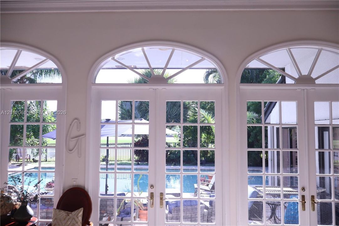 Triple set of French doors featuring multi-pane glass, arched transoms with radial muntins, and metallic hardware