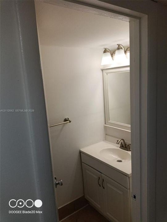Vanity featuring a white cabinet, solid-surface countertop with an integrated oval sink, three-light fixture with white shades, wall-mounted mirror, and brushed-finish faucet