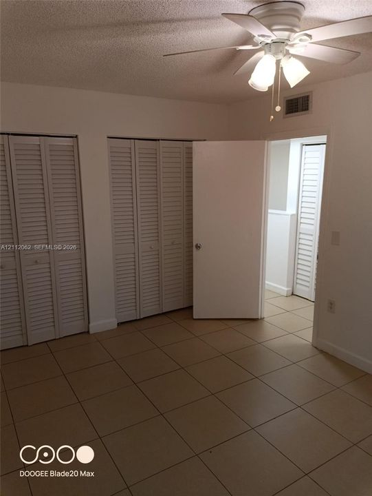 Room featuring neutral ceramic tile flooring, dual floor-to-ceiling closets with louvered bi-fold doors, and a ceiling fan with integrated lighting