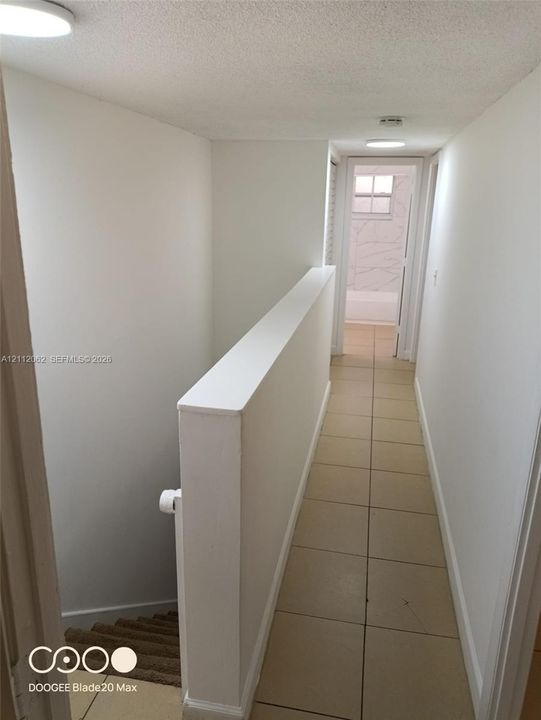 Hallway featuring neutral large-format tile flooring, flush-mount ceiling lighting, and a painted half-wall staircase partition