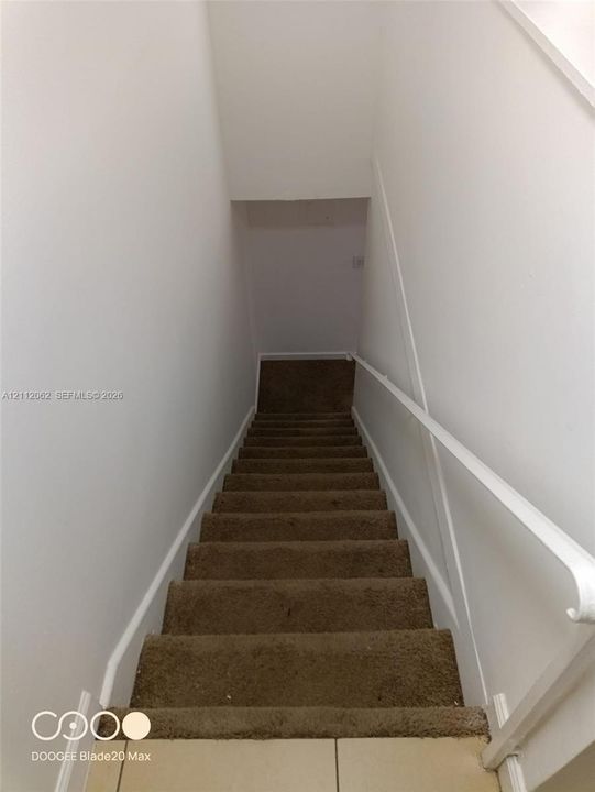 Staircase featuring neutral-toned carpeting and a white wall-mounted handrail