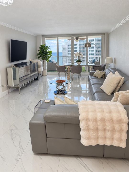 Open-concept living space featuring high-gloss large-format floor tiling, crown molding, floor-to-ceiling glass sliding doors, and a private balcony