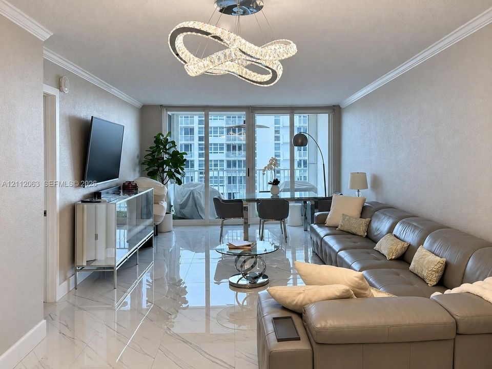 Polished tile flooring with subtle veining, contemporary geometric crystal chandelier, and floor-to-ceiling glass sliding doors opening to a private balcony