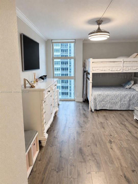 Floor-to-ceiling window, wood-finish flooring, crown molding, and brushed nickel ceiling fan with integrated lighting