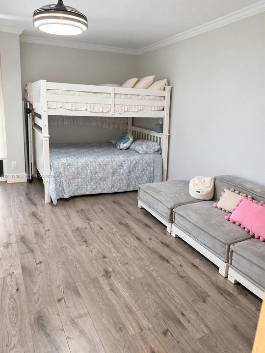 Room featuring wood-finish flooring, crown molding, and a contemporary circular flush-mount ceiling light fixture