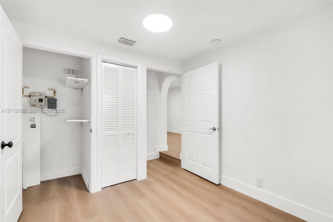 Interior space featuring wood-finish flooring, white paneled doors, louvered closet doors, and an arched architectural opening