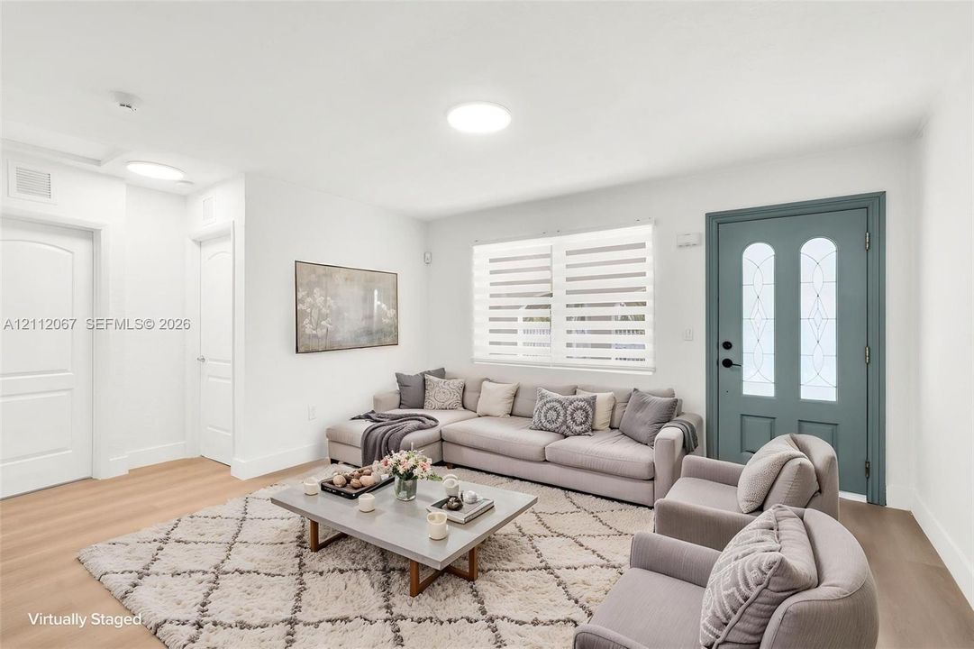 Living area featuring light-toned wood-finish flooring, recessed ceiling lighting, and an exterior door with arched glass inserts