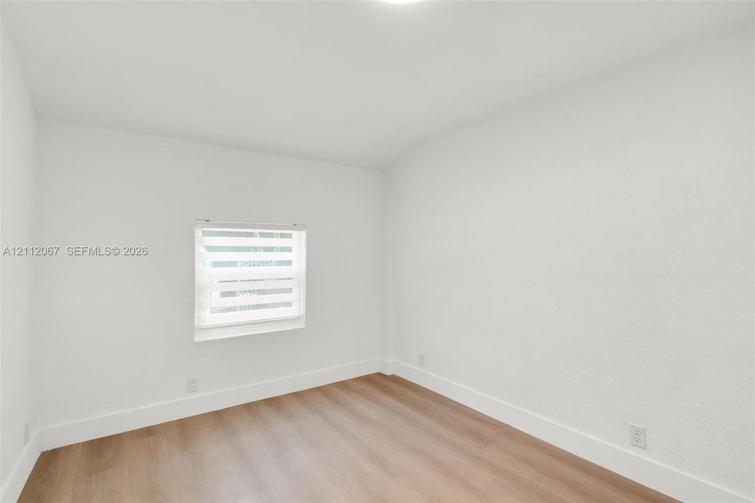 Interior room featuring smooth white walls, wood-finish flooring, and a window with a built-in horizontal shade