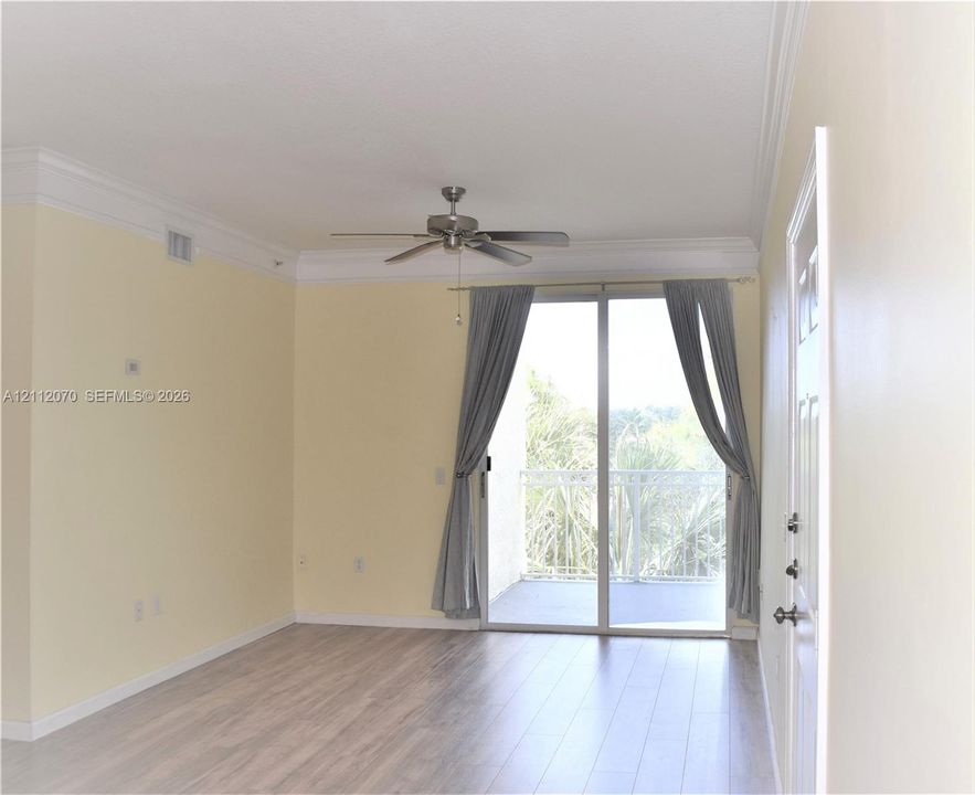 Interior space featuring wood-finish flooring, crown molding, a ceiling fan, and sliding glass doors opening to a balcony
