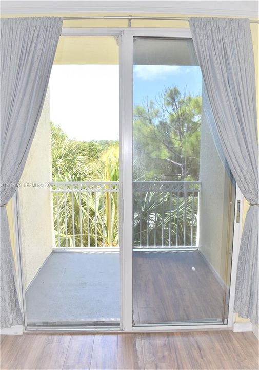Sliding glass door opening to a private balcony with wood-finish flooring and a decorative metal railing