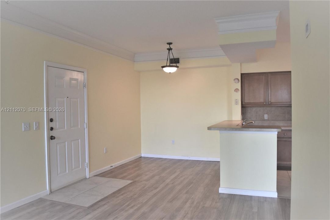 Wood-finish flooring, crown molding, a hanging pendant light fixture, and a breakfast bar with stone-finish countertop
