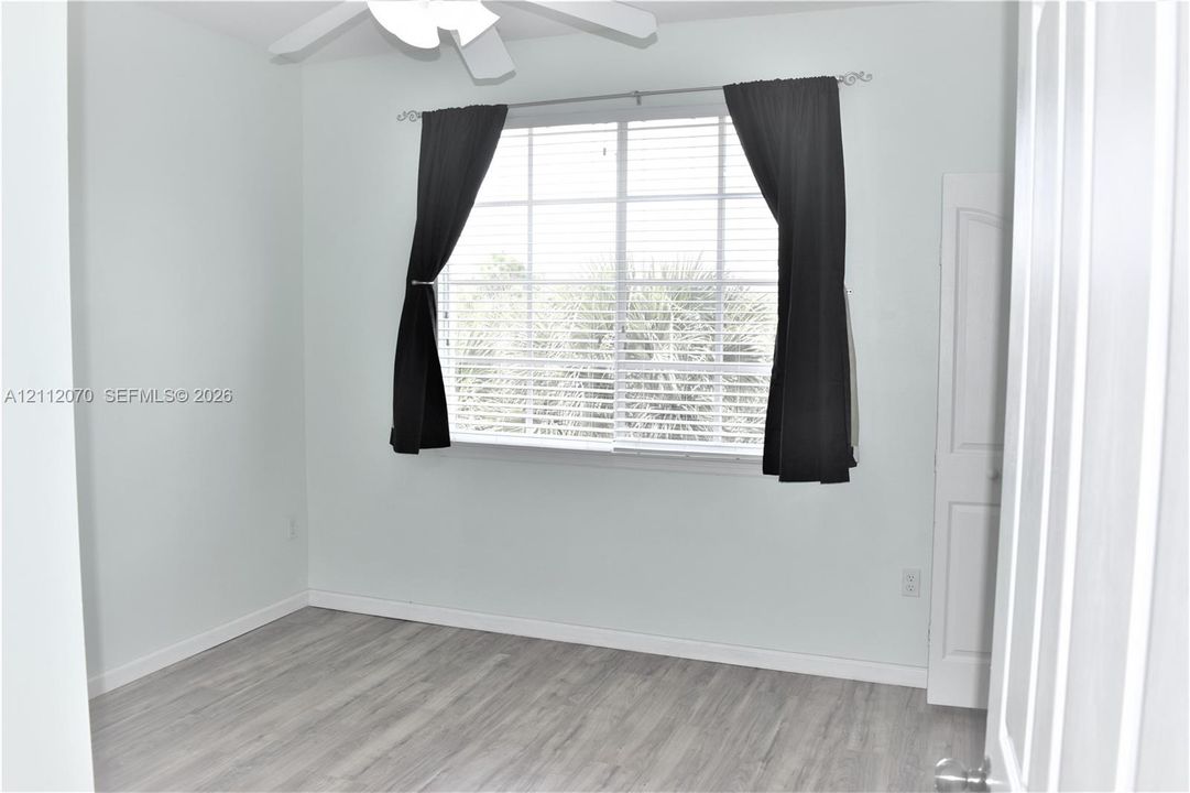 Neutral-toned interior space featuring wood-finish flooring, a ceiling fan, and a large grid-patterned window