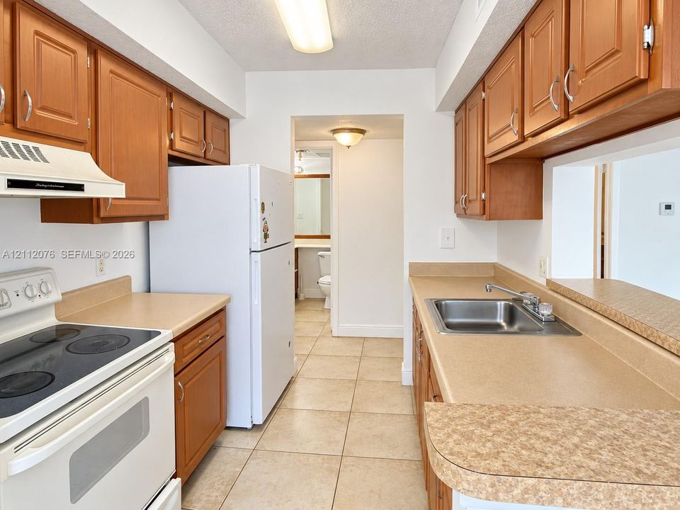 Kitchen featuring wood cabinetry, laminate countertops, tile flooring, and integrated stainless steel sink