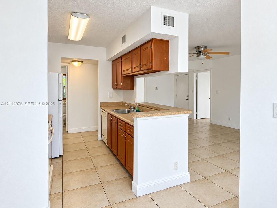 Kitchen featuring wood cabinetry, solid-surface countertops, tile flooring, and integrated white appliances