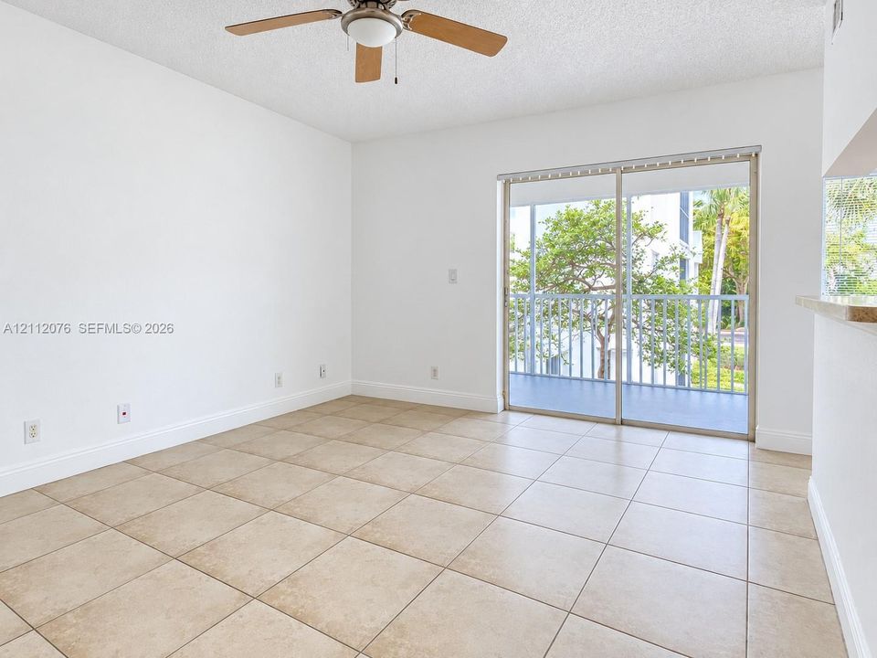 Neutral-toned ceramic tile flooring, ceiling fan with integrated lighting, and glass sliding doors opening to a balcony with metal railings